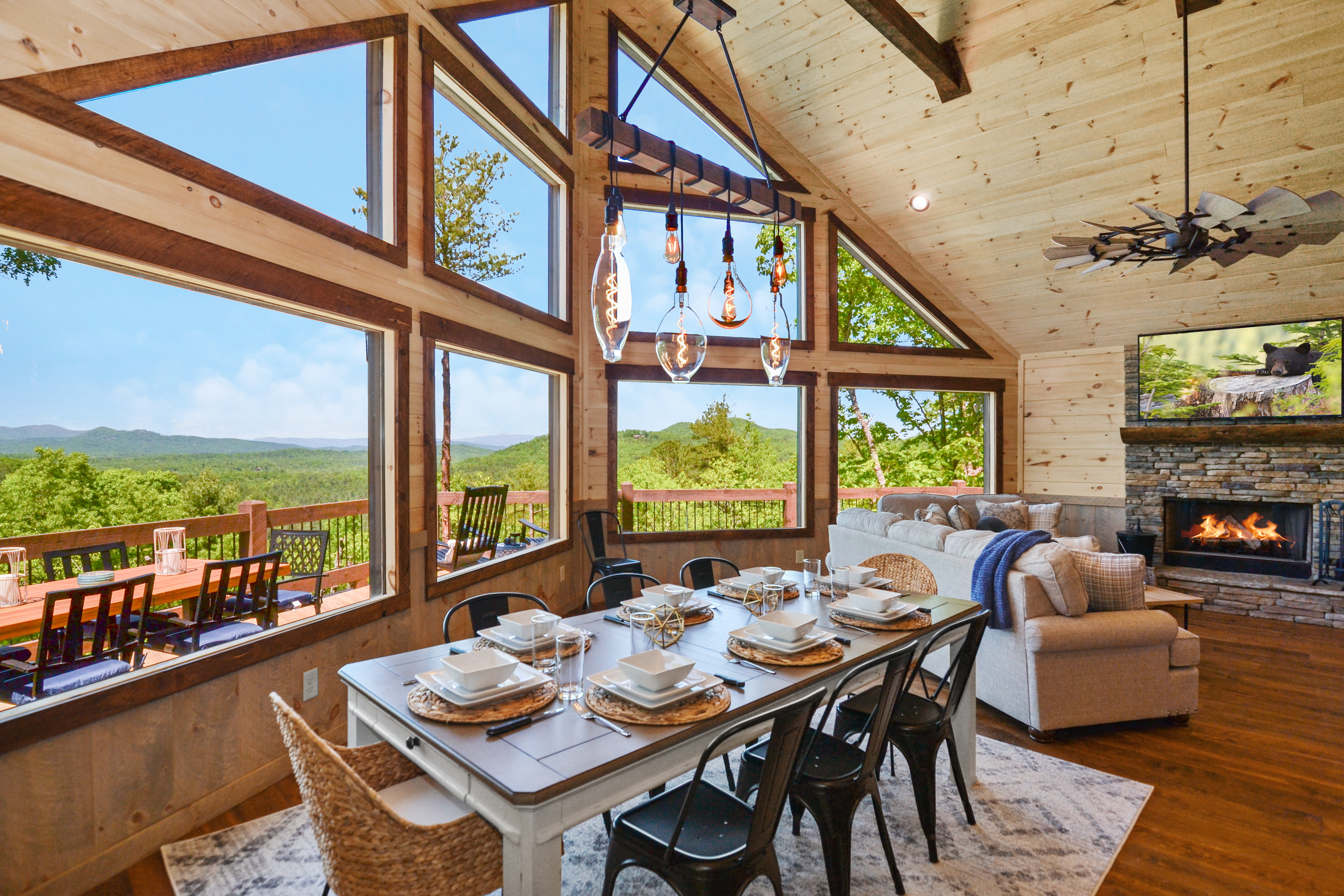 Luxurious cabin interior with open concept kitchen, stone fireplace, and panoramic mountain views